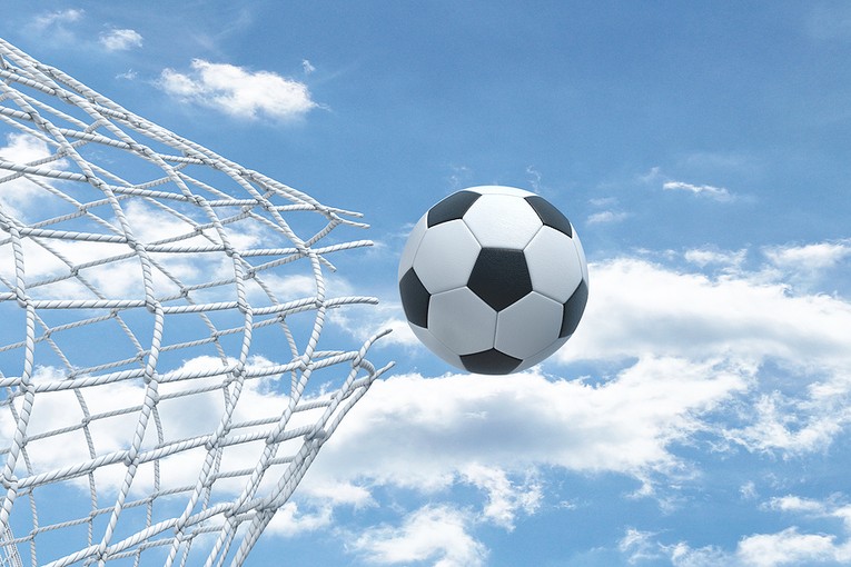 Football Breaking Through Net Against Blue Cloudy Sky