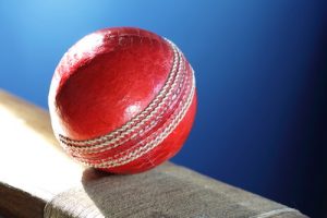Red Cricket Ball on Bat Against Blue Background