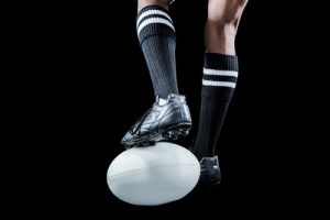 Rugby Player Standing on Ball Against Black Background